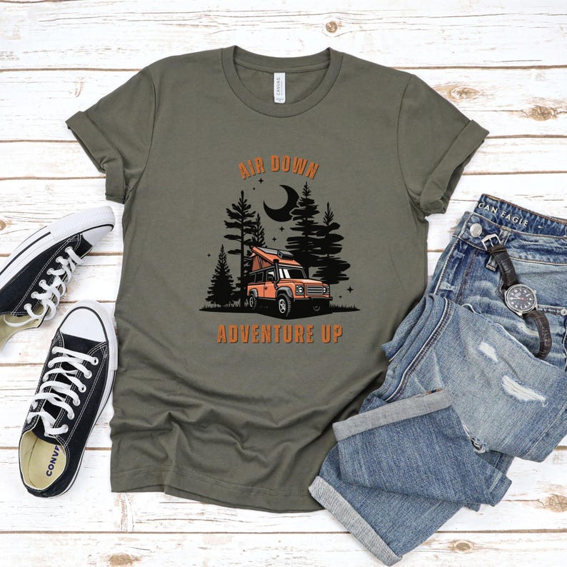 May include: A green t-shirt with the text "Air Down Adventure Up" in orange. The design features a black silhouette of a forest with a moon and a red truck with a pop-up tent.