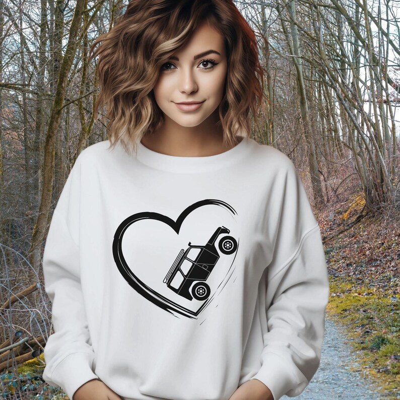 May include: White sweatshirt featuring a black heart with a black off-road vehicle graphic. The vehicle is tilted within the heart shape. The sweatshirt is a casual style, suitable for everyday wear.