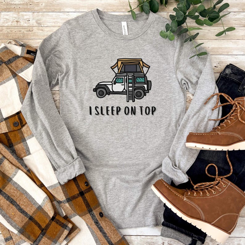 May include: A gray long-sleeved shirt with a white Jeep with a tent on top and the text "I SLEEP ON TOP".