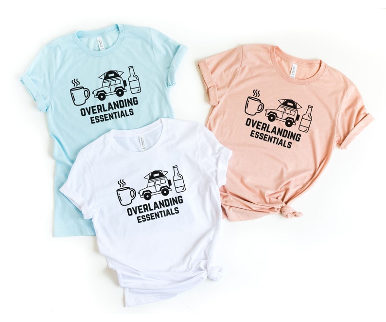 Puede incluir: Tres camisetas con un gr&aacute;fico en blanco y negro de un coche con una tienda de campa&ntilde;a en el techo, una taza de caf&eacute; y una botella de cerveza. El texto en las camisetas dice "Overlanding Essentials". Las camisetas son de color azul claro, melocot&oacute;n y blanco.
