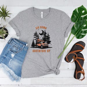 May include: Grey t-shirt with a graphic of a car in a forest with the text "Air Down Adventure Up" printed on it.