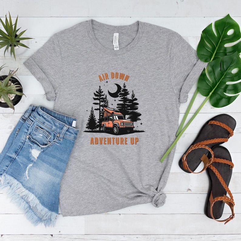 May include: Grey t-shirt with a graphic of a car in a forest with the text "Air Down Adventure Up" printed on it.