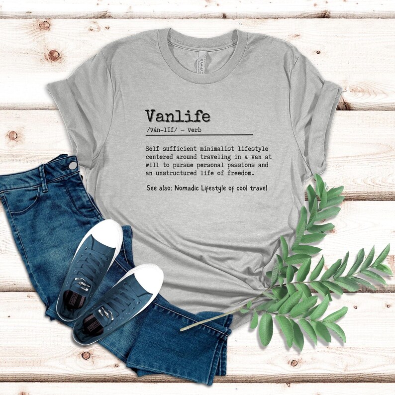 Puede incluir: Una camiseta gris con un dise&ntilde;o gr&aacute;fico negro que define "Vanlife" como un estilo de vida minimalista y autosuficiente centrado en viajar en una furgoneta. El texto tambi&eacute;n incluye la pronunciaci&oacute;n fon&eacute;tica de la palabra "Vanlife" y una descripci&oacute;n del estilo de vida.