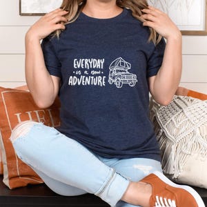 May include: A navy blue t-shirt with a white graphic of a camper van with a tent on top. The text "EVERYDAY is a new ADVENTURE" is printed on the shirt.