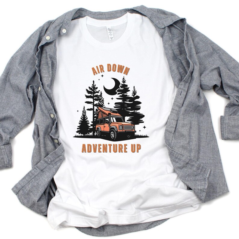 May include: White t-shirt featuring a graphic of a camper van in a forest at night. The text "Air Down Adventure Up" is printed on the shirt.
