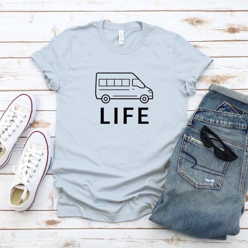 Op de afbeelding: Lichtblauw T-shirt met een zwarte omtrek van een bestelwagen en het woord "LIFE" erop gedrukt.