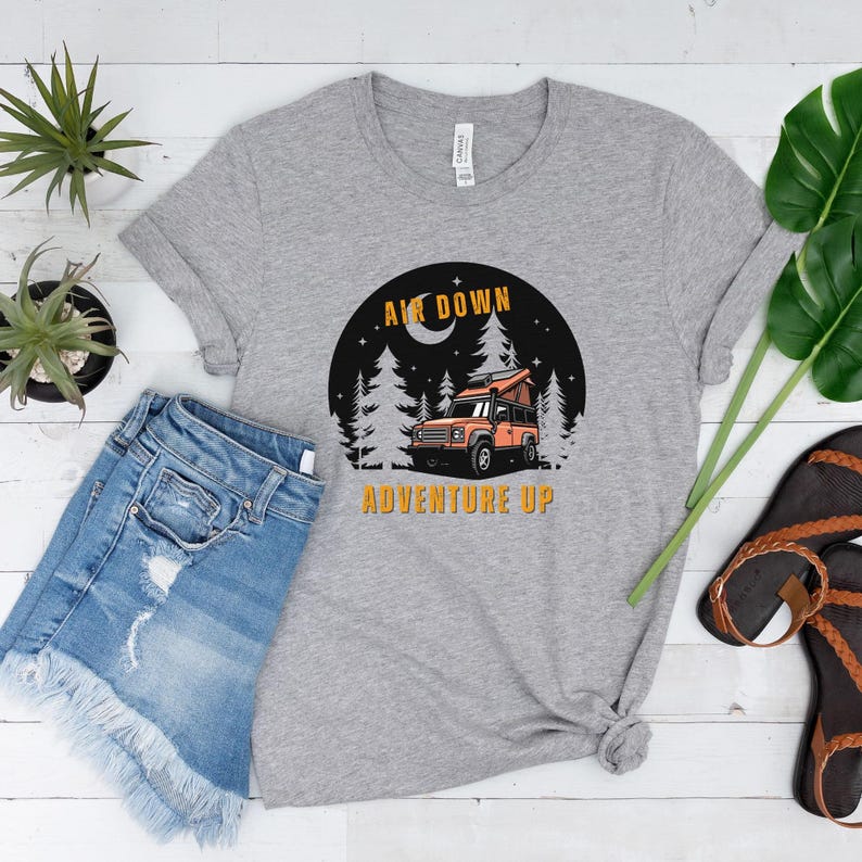 Puede incluir: Camiseta gris con un gr&aacute;fico de un coche en un bosque con el texto "Air Down Adventure Up" impreso en ella.