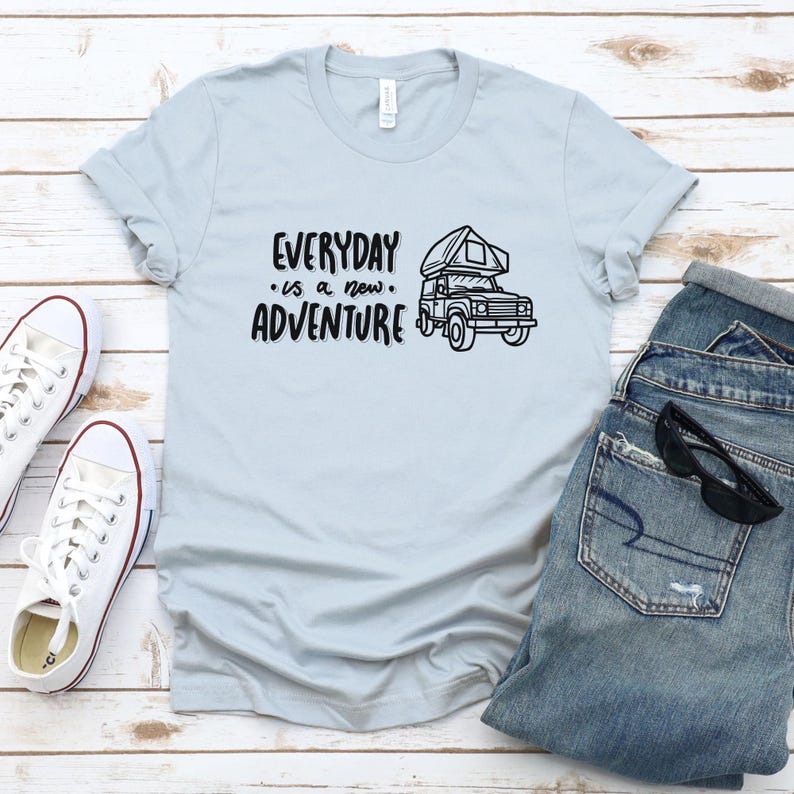 Może przedstawiać: Jasnoniebieska koszulka z czarnym nadrukiem kampera i tekstem "EVERYDAY is a new ADVENTURE".