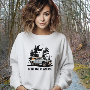 May include: White sweatshirt with a black graphic of a truck with a camper shell driving through a forest at night. The text "Gone Overlanding" is below the graphic.