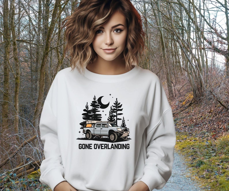 May include: White sweatshirt with a black graphic of a truck with a camper shell driving through a forest at night. The text "Gone Overlanding" is below the graphic.