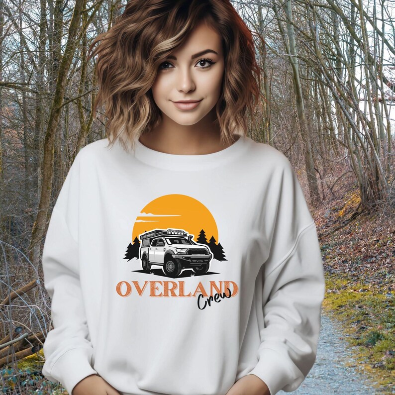 May include: White sweatshirt featuring an orange sunset graphic and a white truck with a roof rack. The text "OVERLAND Crew" is printed in orange below the truck.