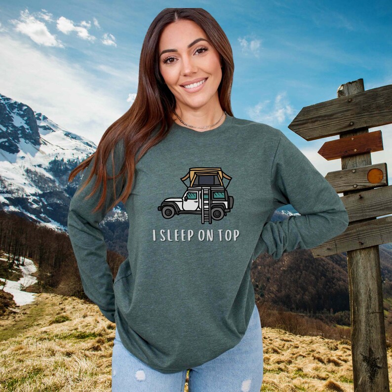 May include: A green long-sleeved shirt with a cartoon illustration of a car with a tent on top. The text "I SLEEP ON TOP" is printed below the car.