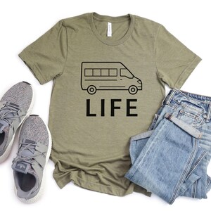 Op de afbeelding: Een groen T-shirt met een zwarte omtrek van een bestelwagen en het woord "LIFE" erop gedrukt.