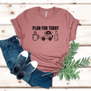 May include: A pink t-shirt with the text "PLAN FOR TODAY" in black lettering. The design includes a coffee cup, a car with a tent on top, and a bottle of beer.