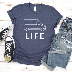 Op de afbeelding: Een marineblauw t-shirt met een witte omtrek van een bestelwagen en het woord "LIFE" gedrukt op de voorkant.
