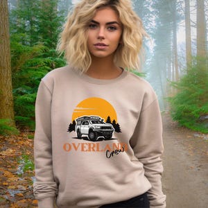 May include: A beige sweatshirt featuring an orange sun and a white truck with a roof rack. The text "Overland Crew" is printed in orange below the truck.