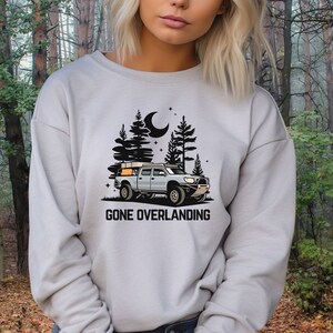 May include: A gray sweatshirt with a black graphic of a truck with a rooftop tent driving through a forest at night. The text "Gone Overlanding" is printed below the truck.
