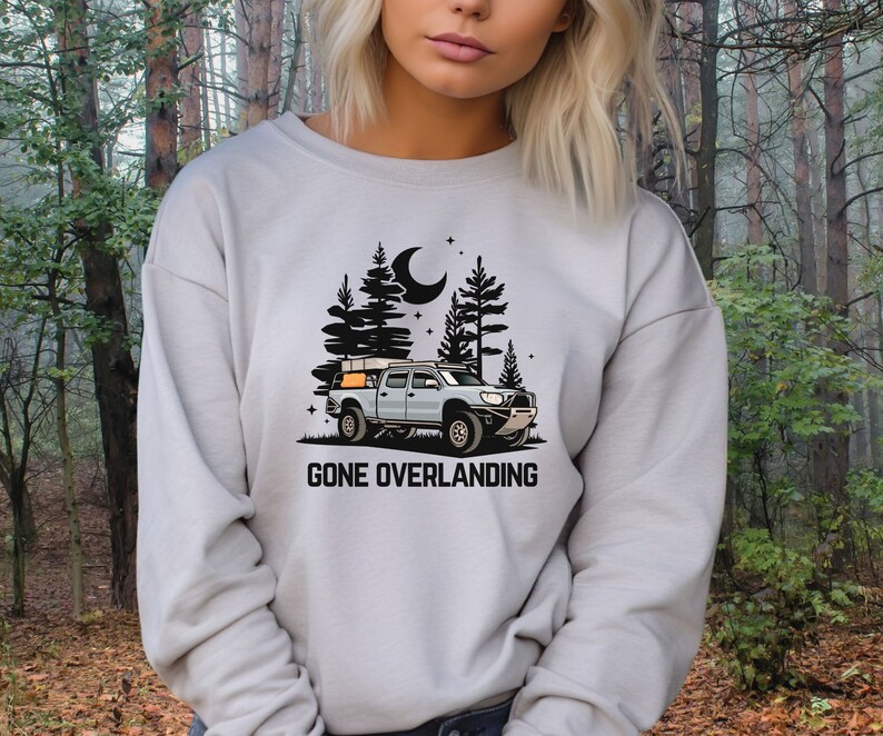 May include: A gray sweatshirt with a black graphic of a truck with a rooftop tent driving through a forest at night. The text "Gone Overlanding" is printed below the truck.