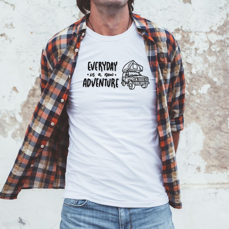 May include: White t-shirt with a black graphic of a camper van and the text "EVERYDAY is a new ADVENTURE". The person is wearing a red and black plaid shirt.