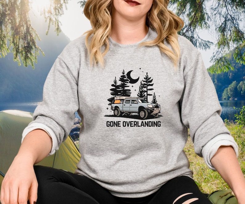 May include: A gray sweatshirt with a black graphic of a truck with a rooftop tent driving through a forest at night. The text "Gone Overlanding" is printed below the truck.