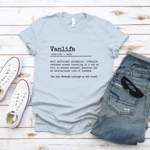 Puede incluir: Una camiseta azul claro con la palabra "Vanlife" definida como un "estilo de vida minimalista autosuficiente centrado en viajar en una furgoneta a voluntad para perseguir pasiones personales y una vida no estructurada de libertad." El texto tambi&eacute;n dice "Ver tambi&eacute;n: Estilo de vida n&oacute;mada de viajes geniales."