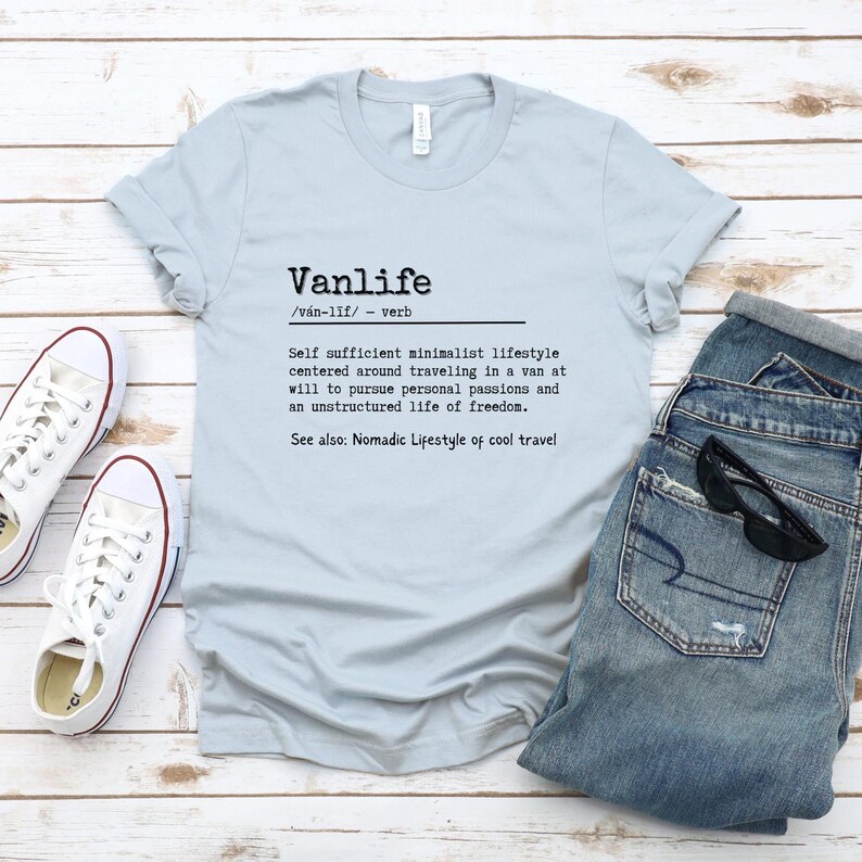 Puede incluir: Una camiseta azul claro con la palabra "Vanlife" definida como un "estilo de vida minimalista autosuficiente centrado en viajar en una furgoneta a voluntad para perseguir pasiones personales y una vida no estructurada de libertad." El texto tambi&eacute;n dice "Ver tambi&eacute;n: Estilo de vida n&oacute;mada de viajes geniales."