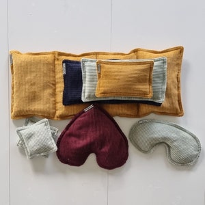 Peut inclure: Divers coussins en velours côtelé de différentes formes et tailles. Les couleurs incluent le jaune moutarde, le bleu marine, le bordeaux et le vert clair. Certains coussins sont rectangulaires, d'autres en forme de cœur ou incurvés.