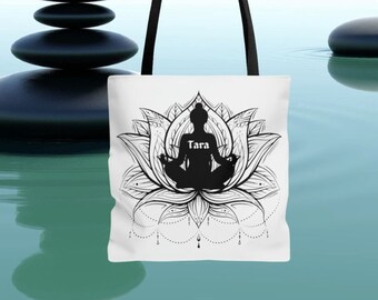 May include: White tote bag with black handles and a black and white design of a person meditating in a lotus flower with the word "Tara" written below.