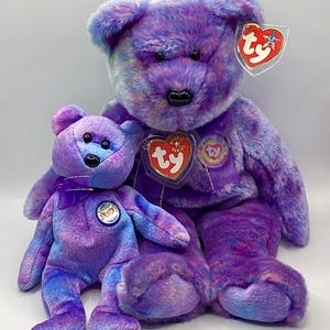 May include: Two purple and blue tie-dye beanie babies. The larger beanie baby has a red "Ty" tag with a star and a red heart tag with a "Ty" logo. The smaller beanie baby has a purple ribbon around its neck and a blue "Ty" tag with a star.