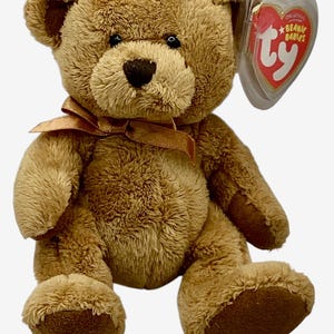 May include: A brown plush teddy bear with a satin ribbon around its neck. The bear has a heart-shaped tag that reads "Beanie Babies" in red and white. The bear is sitting upright with its arms and legs extended.