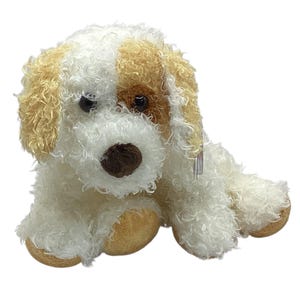 May include: A plush dog toy featuring curly white fur with tan patches on the ears and around one eye. The stuffed animal has a dark brown nose, black plastic eyes, and tan-colored paws, presented in a seated position with a small tag attached.