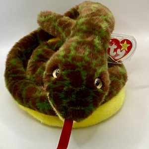 May include: Green and brown snake plush toy with a yellow belly and a red tongue. The toy has a Ty tag attached to it.