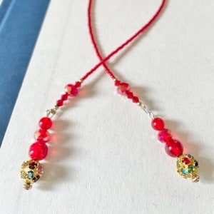 May include: A red beaded bookmark with gold-toned beads and a crystal embellishment at each end.