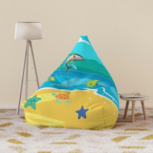 Può includere: Una poltrona sacco gialla e blu con un design a tema spiaggia. Il design presenta una tartaruga, una stella marina e pesci che nuotano nell'oceano.