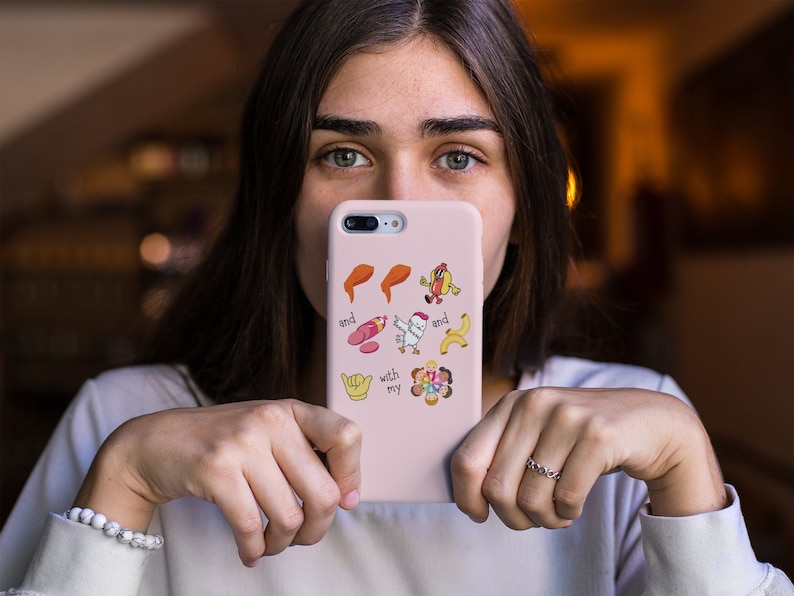 May include: A pink phone case with a variety of colorful stickers, including a chicken, a hot dog, a banana, a hand with a thumbs up, and a peace sign. The text "and my" is visible on the case.