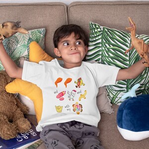 May include: A white t-shirt with a colorful graphic design featuring a chicken, hot dog, banana, and other food items. The text on the shirt reads "and with my".