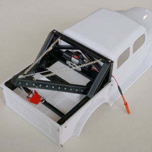 May include: White toy truck with a black metal frame and a winch on the back. The truck has a red and black winch cable.