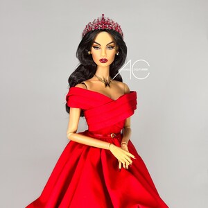 May include: A doll wearing a red off-the-shoulder gown with a gold belt, a jeweled crown, and a gold necklace. The doll has long black hair and dark makeup.