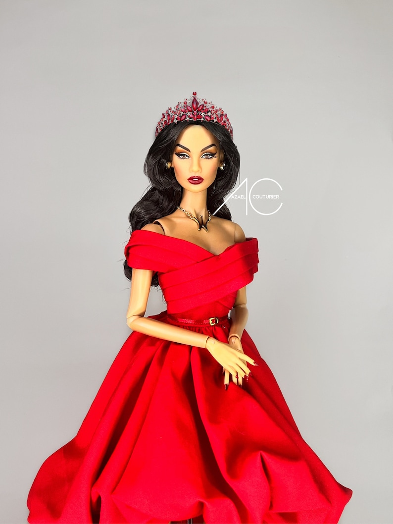 May include: A doll wearing a red off-the-shoulder gown with a gold belt, a jeweled crown, and a gold necklace. The doll has long black hair and dark makeup.