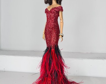Puede incluir: Un vestido rojo de lentejuelas con escote de corazón y tirantes de hombros descubiertos. El vestido tiene una larga cola de plumas rojas y negras.