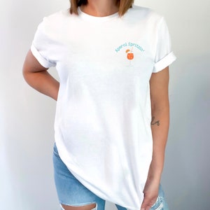 May include: White t-shirt with a blue and orange graphic of a cocktail glass with the text "Aperol Spritz!"