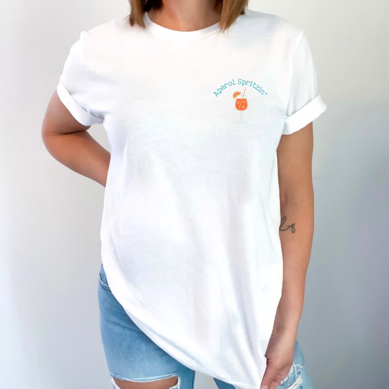 May include: White t-shirt with a blue and orange graphic of a cocktail glass with the text "Aperol Spritz!"