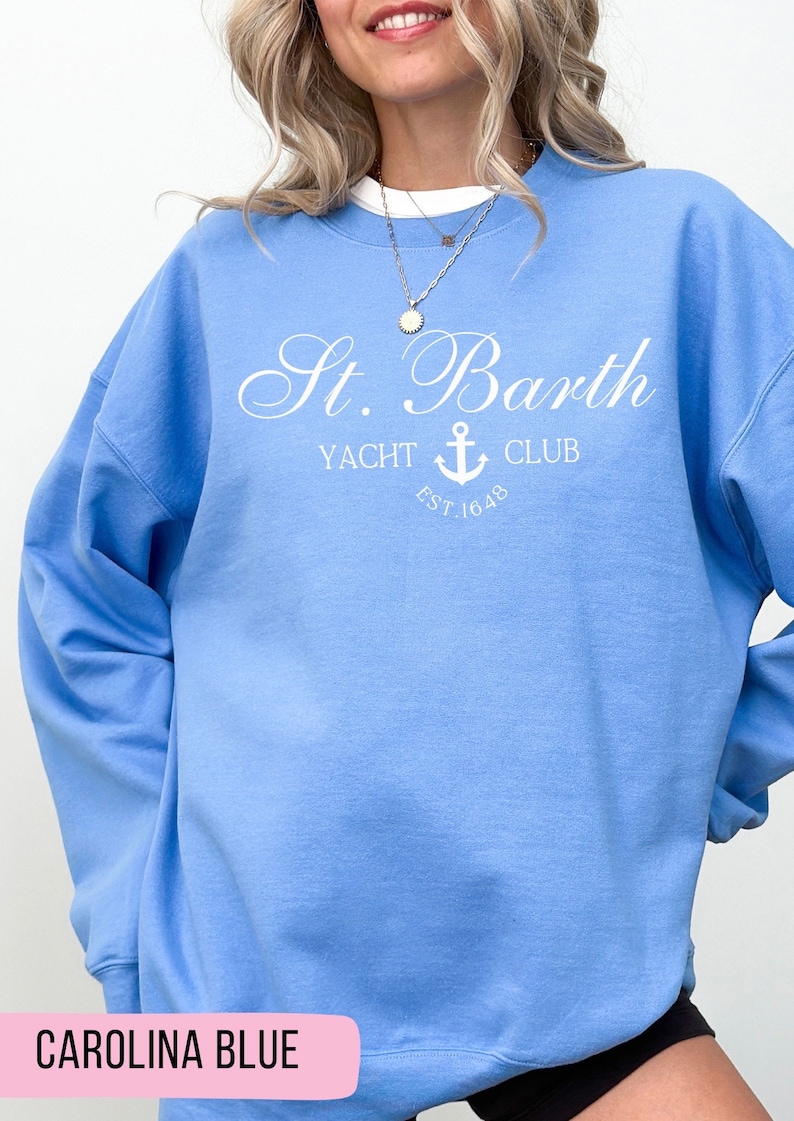 May include: A light blue sweatshirt with the text "St. Barth Yacht Club Est. 1648" in white. The text is in a cursive font and features an anchor symbol.