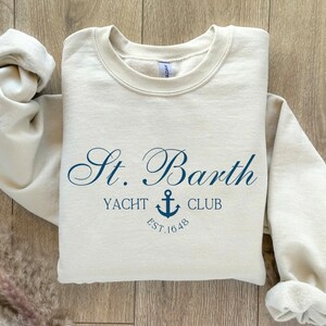 May include: A beige sweatshirt with a navy blue graphic that says "St. Barth Yacht Club Est. 1648" with an anchor symbol.