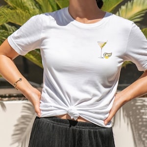 Puede incluir: Camiseta blanca con un gr&aacute;fico de una copa de martini con una aceituna y una rodaja de lim&oacute;n.