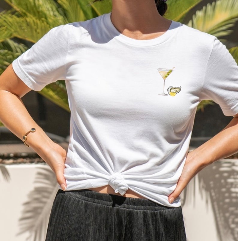 Puede incluir: Camiseta blanca con un gr&aacute;fico de una copa de martini con una aceituna y una rodaja de lim&oacute;n.
