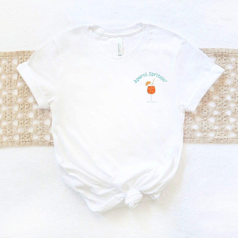 May include: White t-shirt with a graphic of an Aperol Spritz cocktail and the text "Aperol Spritzin'" in turquoise.