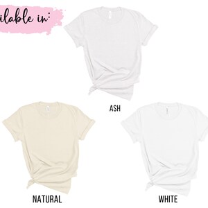 Peut inclure: Trois t-shirts de couleurs diff&eacute;rentes&nbsp;: gris cendr&eacute;, naturel et blanc. Les t-shirts sont pos&eacute;s &agrave; plat et ont un aspect nou&eacute;. Le texte "Available in&nbsp;:" est &eacute;crit en rose en haut de l&rsquo;image.