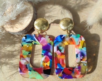 May include: A pair of colorful, rectangular earrings with a gold-colored circular stud. The earrings feature a vibrant mix of colors including blue, purple, green, and red. The earrings have a cut-out rectangle in the center.