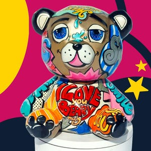 Könnte beinhalten: Dekorative Bärenfigur mit braunem Gesicht, blauen Augen und schwarzen Ohren. Der Bär ist mit Graffiti-Kunst verziert, einschließlich des Textes "I Love You Beary Much" auf der Brust. Der Hintergrund ist eine Mischung aus Pink, Gelb und Marineblau.